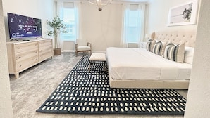 A bedroom with a bed, a TV, a chair, a plant, and a chandelier. - Luxury 6 bed South-Facing Pool, Game Room, 4 Miles to Disney World (Kissimmee)