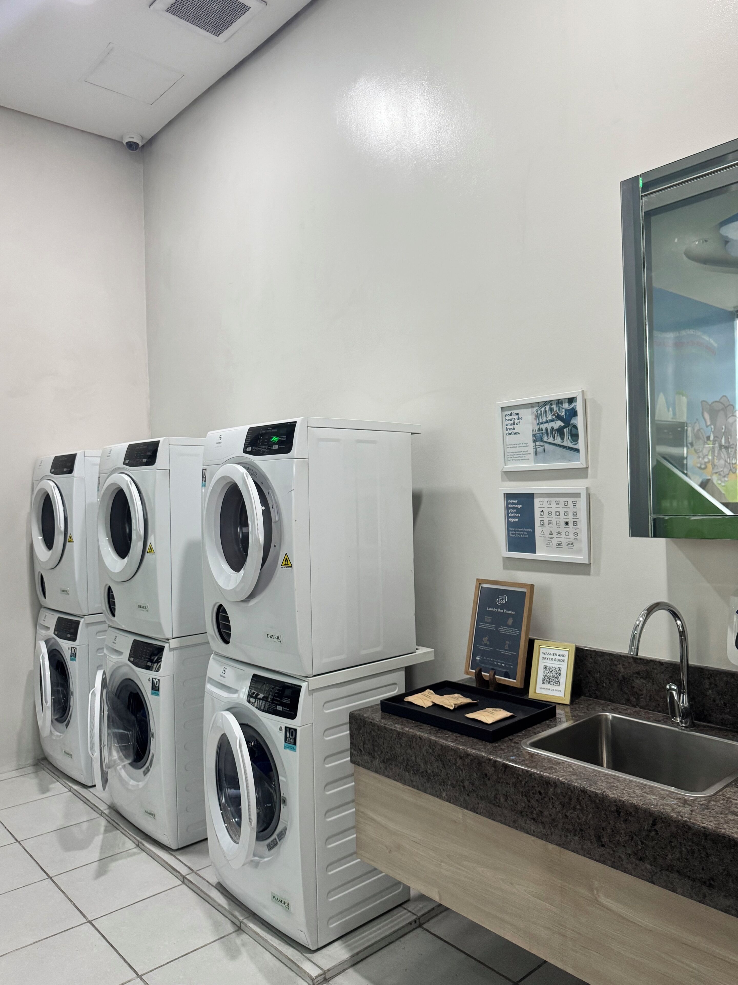 Un lavadero con lavadoras apiladas, un lavabo y carteles informativos en la pared.