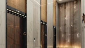Un ascenseur moderne doté de panneaux en bois, d’un sol en marbre poli et d’un mur décoratif orné de lignes verticales.