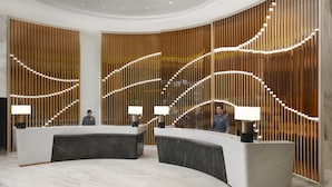 Un espace d’accueil moderne avec un comptoir en marbre incurvé, deux lampes et un mur en panneaux de bois doté d’un éclairage intégré.