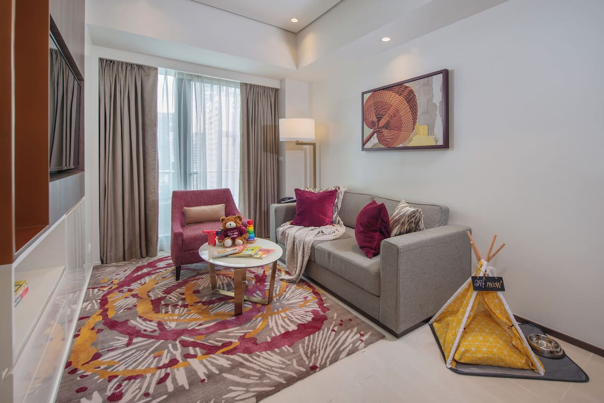 Ein modernes Wohnzimmer mit grauem Sofa, einem Teppich mit roten und gelben Mustern, einem kleinen runden Tisch, einem Teddybären und einem gelben Teepee.