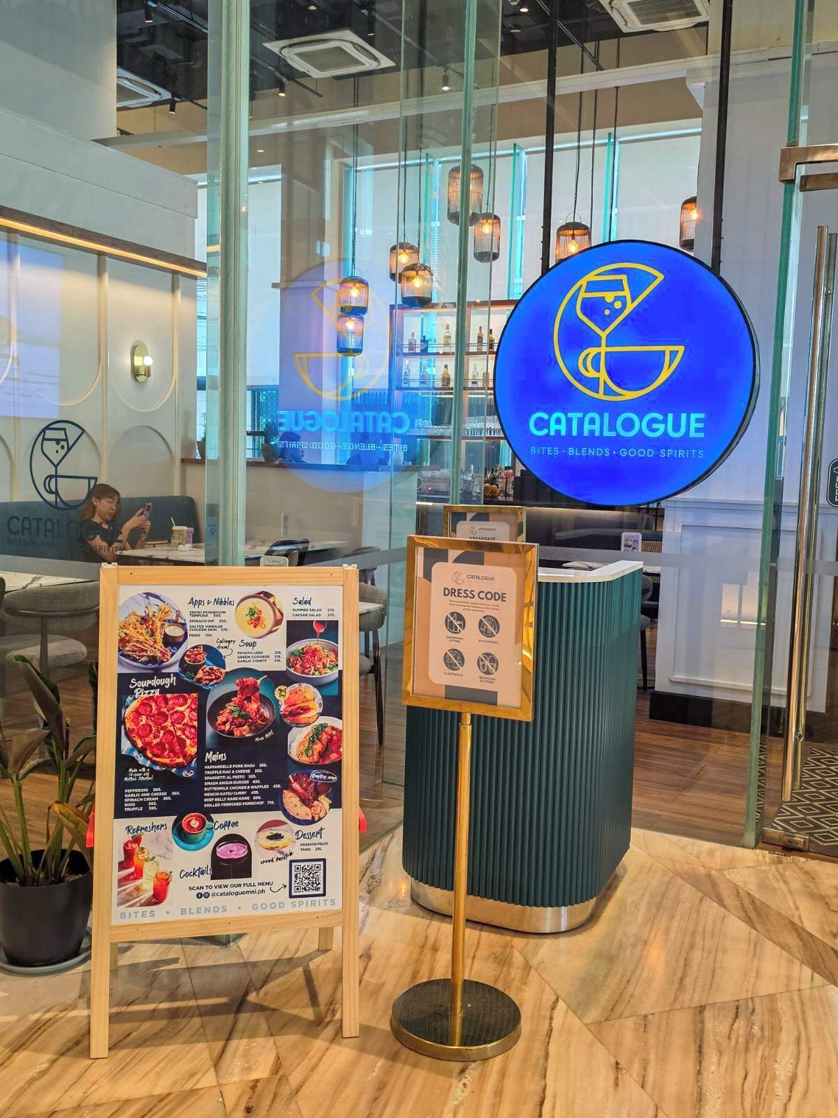 Een modern café interieur met een menubord, een bord met kledingvoorschriften en een blauw logo.