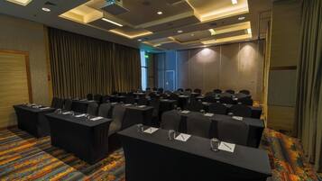 Un salón de conferencias con filas de mesas y sillas, una alfombra estampada y un diseño moderno de techo.