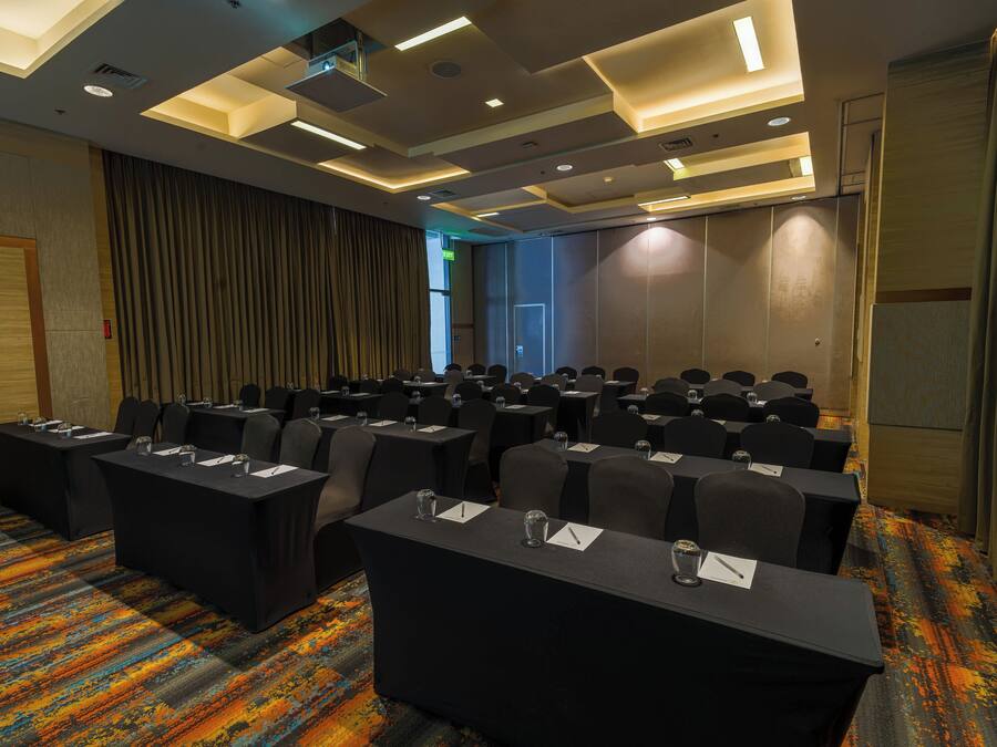 Un salón de conferencias con filas de mesas y sillas, una alfombra estampada y un diseño moderno de techo.
