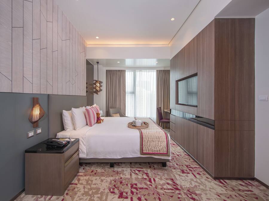 A modern hotel room with a large bed, a bedside table, a TV, and a wardrobe.
