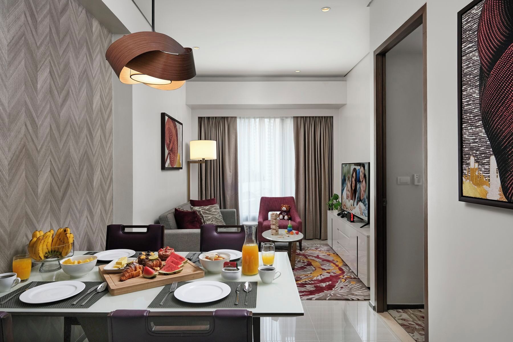 A modern hotel room with a dining area, a sofa, a TV, and a painting on the wall.