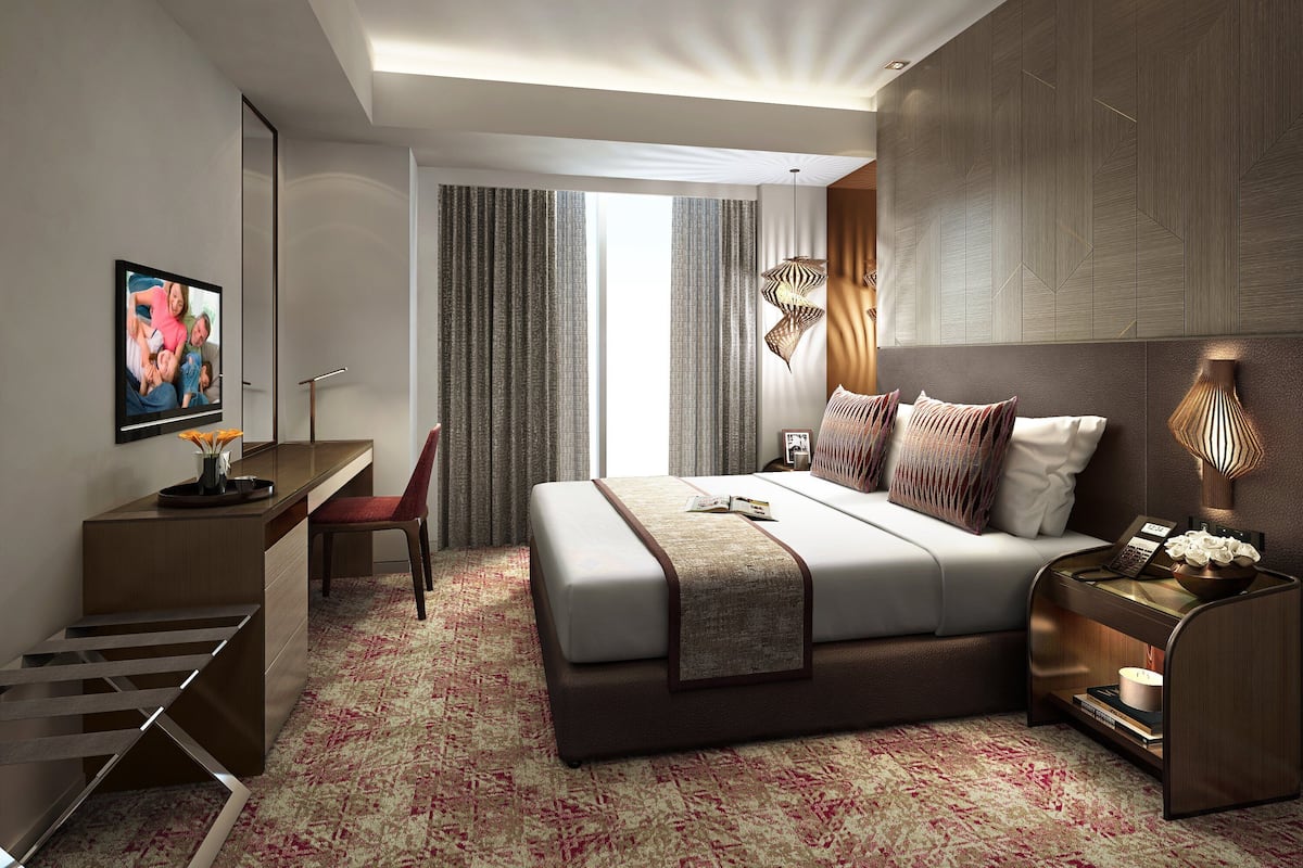 Ein modernes Hotelzimmer mit einem großen Bett, einem Schreibtisch und einem Stuhl. An der Wand befindet sich ein Fernseher und ein Fenster mit Vorhängen.