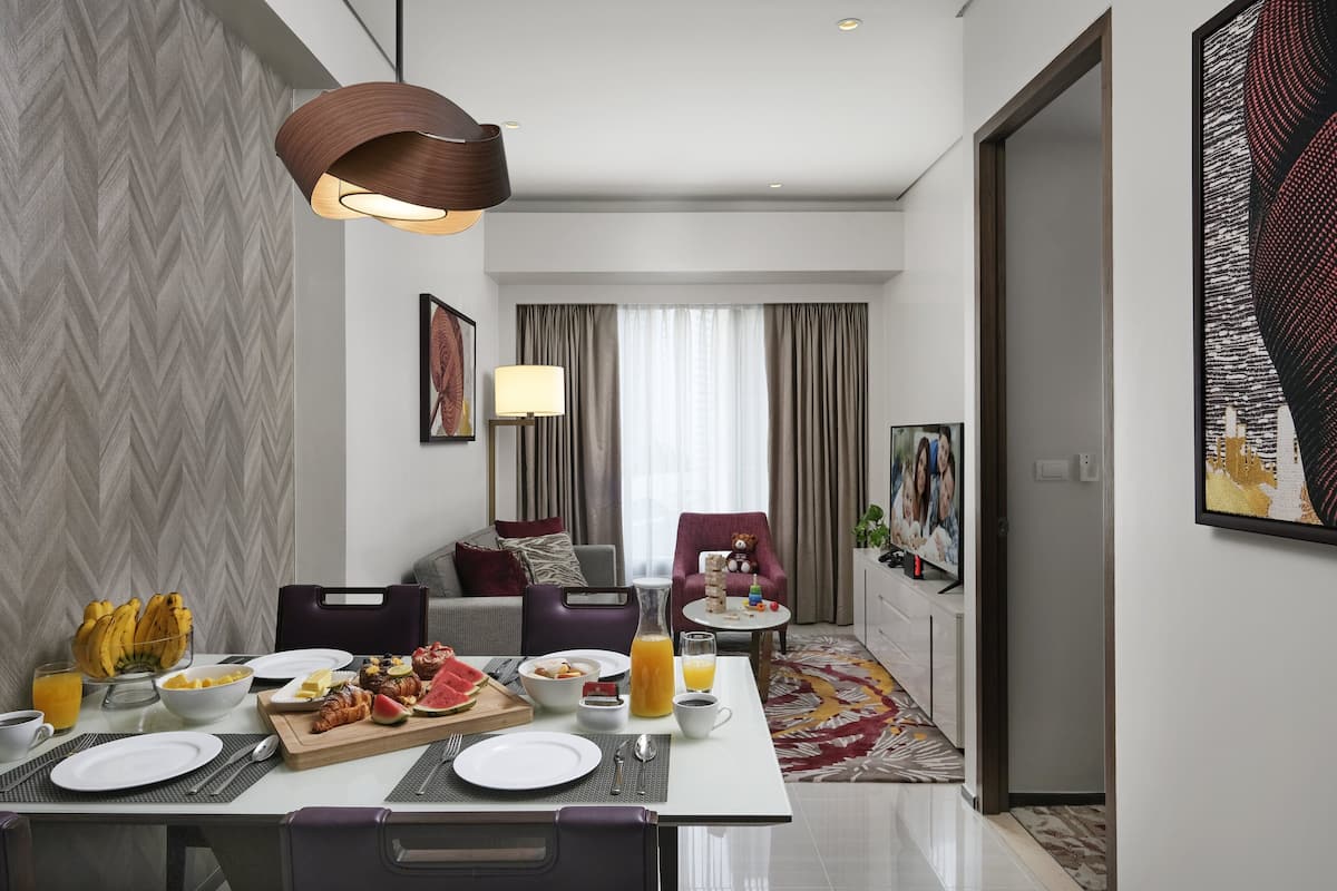Ein modernes Hotelzimmer mit Essbereich und Frühstücksecke, inklusive Tellern, Besteck und Obstschale.