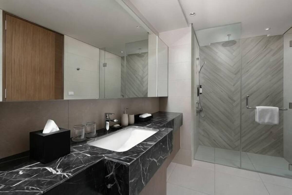 Ein modernes Badezimmer mit Marmorwaschbecken, einem großen Spiegel und einer Duschwand mit Fischgrätenmuster.