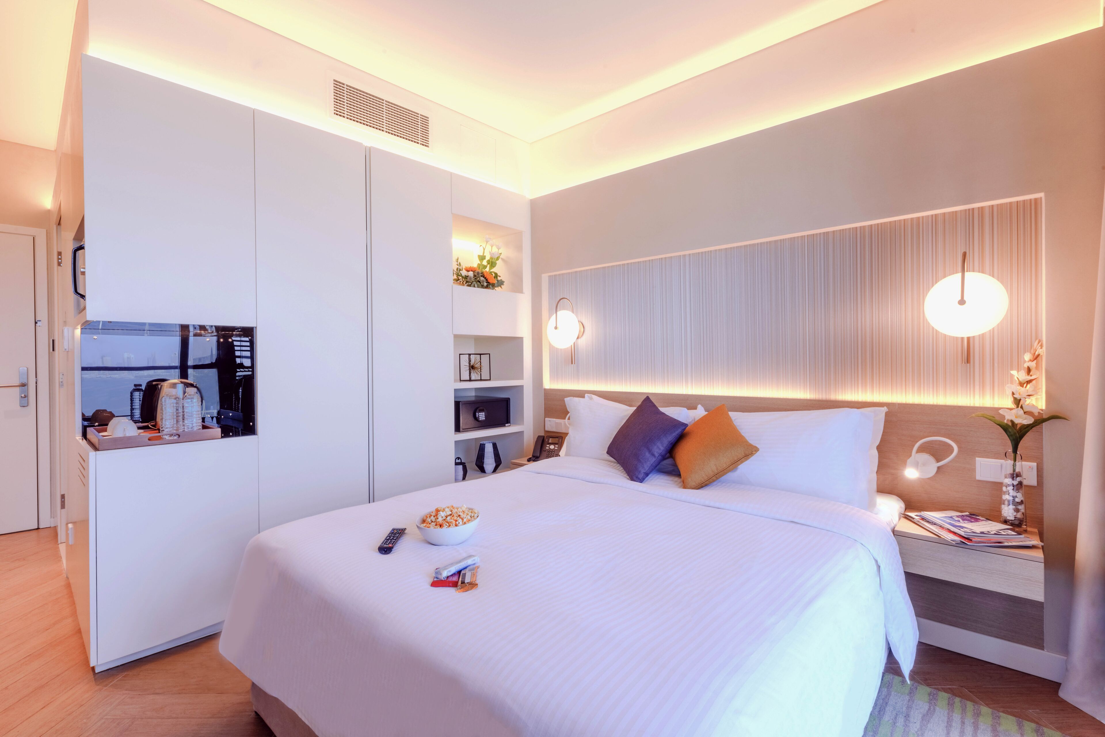 A modern hotel room with a large bed, a built-in TV, a microwave, and a small kitchenette.