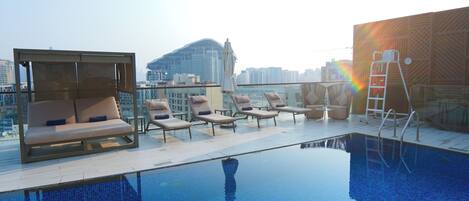 A rooftop pool area with lounge chairs and a view of a city skyline.