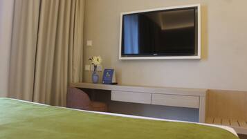 Habitación de hotel con cama, escritorio con televisor de pantalla plana, una silla y un florero con flores.