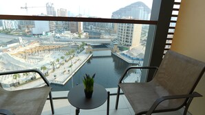 Un balcón con dos sillas y una pequeña mesa, con vistas a un paisaje urbano que incluye un río y zonas de construcción.