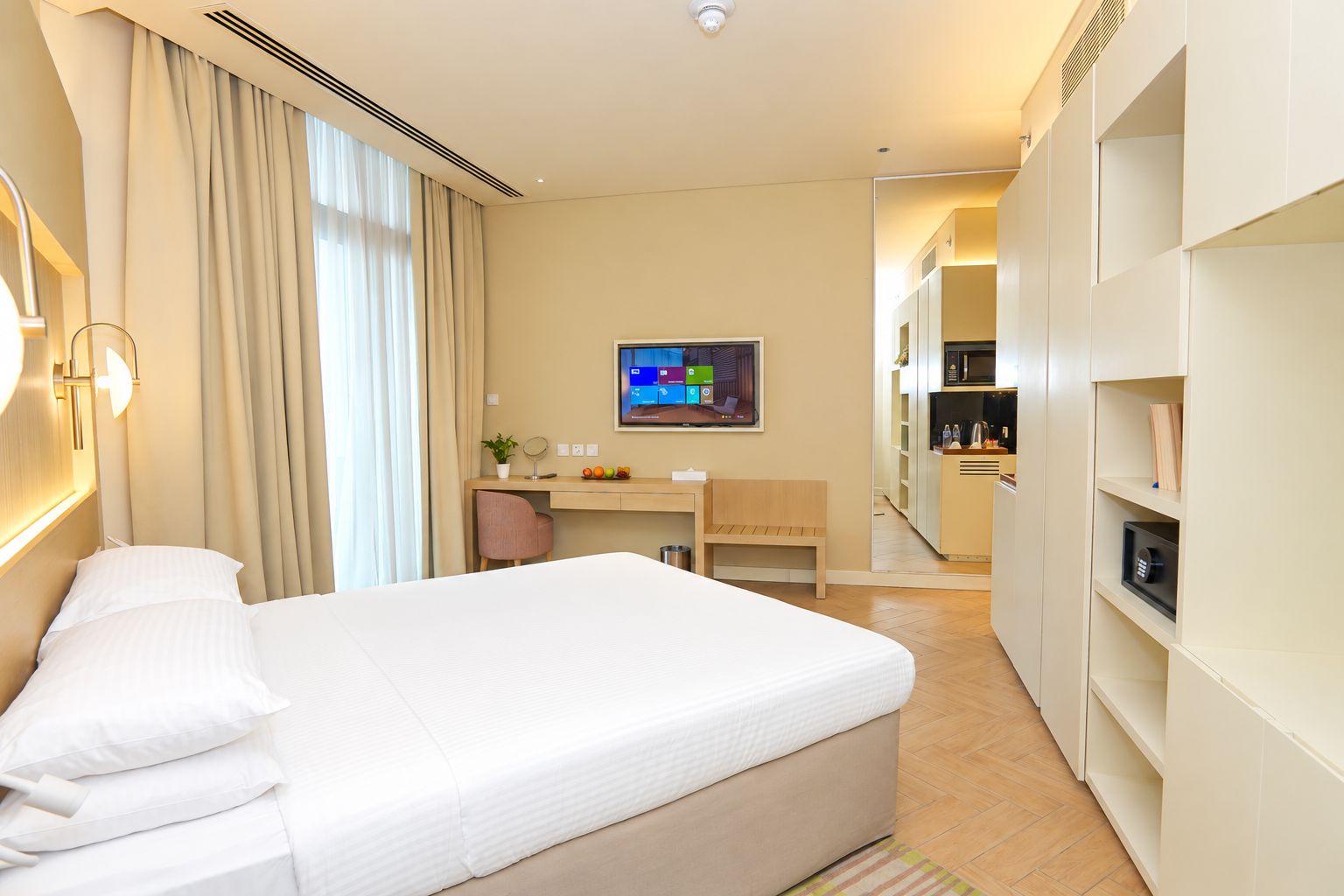 A hotel room with a bed, a desk, a chair, a television, and a kitchenette.