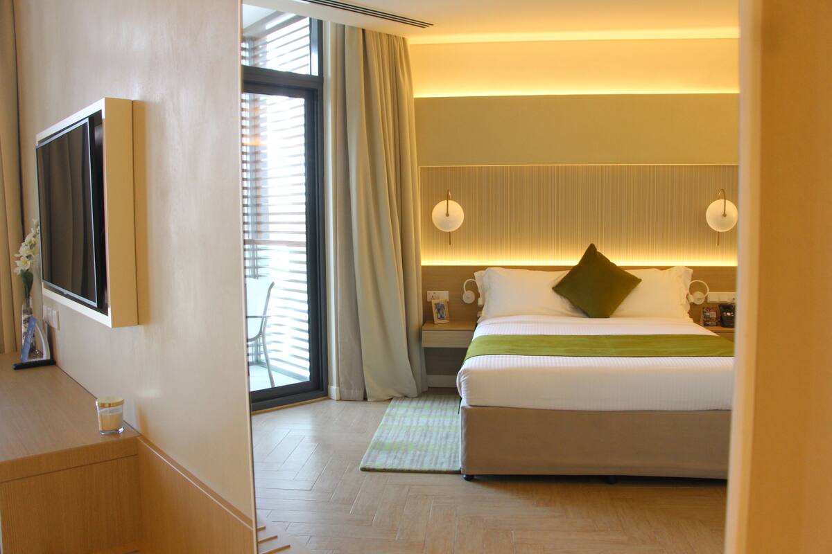 A hotel room with a bed, bedside tables, a TV, and a window with curtains.