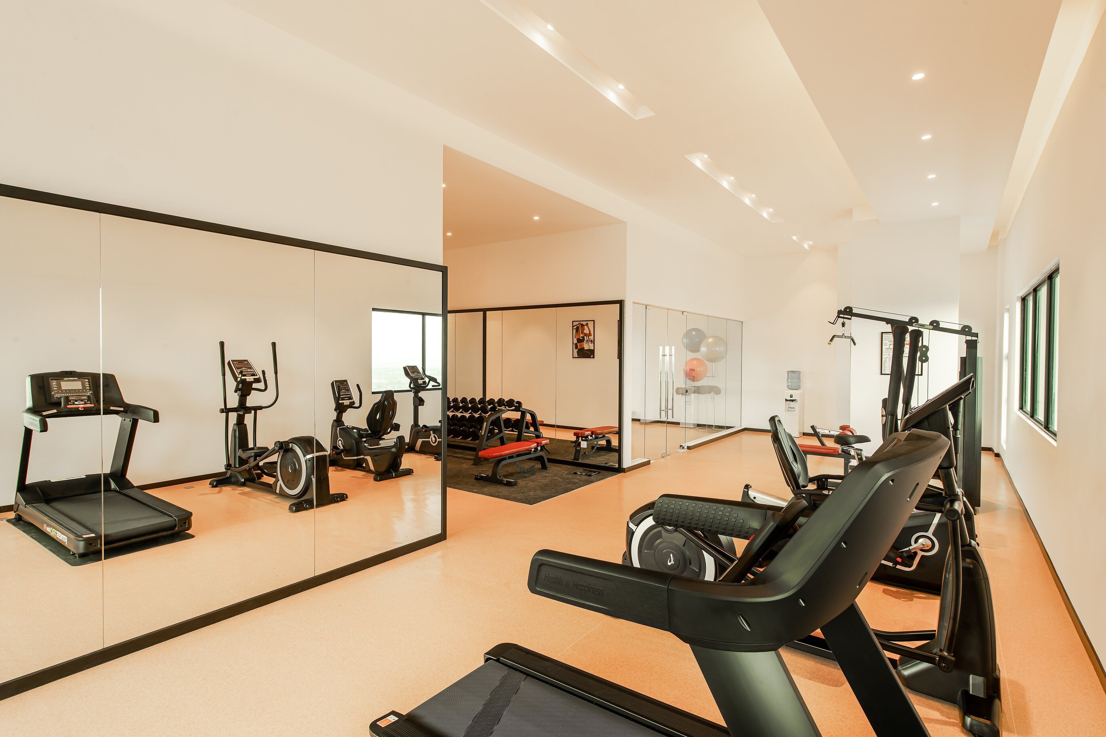 Un gimnasio con equipo de ejercicio, un espejo grande y una banca.