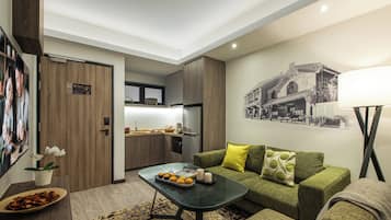 Ein modernes Wohnzimmer mit einem grünen Sofa, einem Couchtisch mit Snacks, einer sichtbaren Küche im Hintergrund und einer Wandlampe.