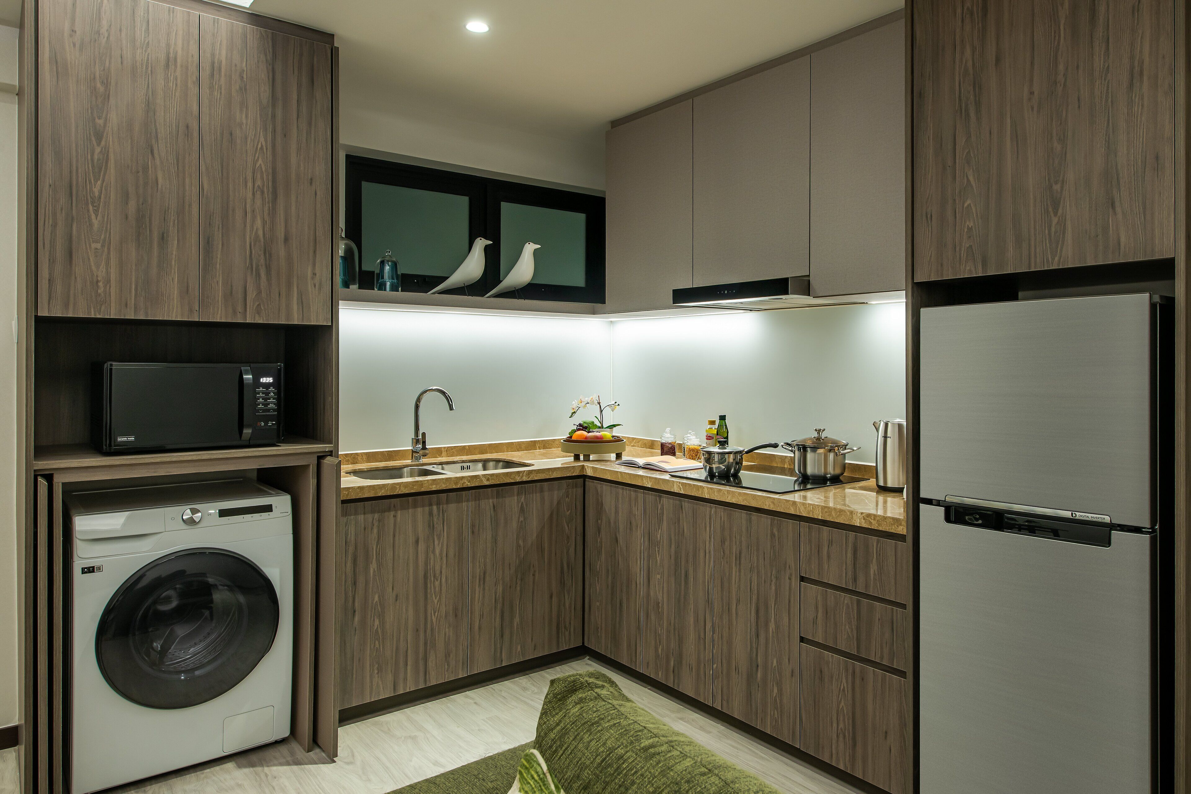 Een kleine keuken met een wasmachine, magnetron, spoelbak en een koelkast van roestvrij staal.