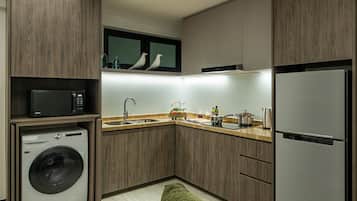Een kleine keuken met een wasmachine, magnetron, spoelbak en een koelkast van roestvrij staal.
