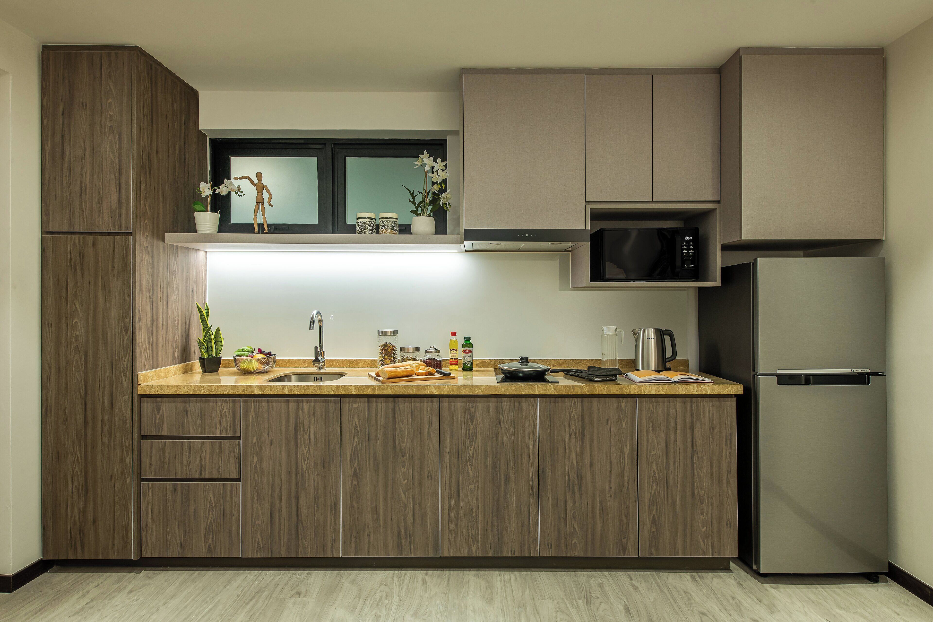 A modern kitchen with wooden cabinets, a stainless steel refrigerator, a microwave, and a window above the sink.