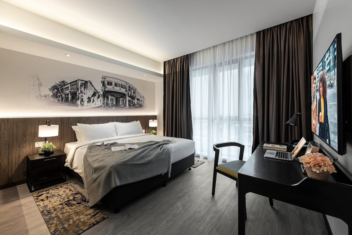 A modern hotel room with a neatly made bed, a desk with a laptop, and a large window with curtains.