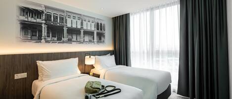 Habitación de hotel con dos camas, un ventanal con cortinas, una lámpara fijada a la pared y un cuadro con la imagen de un edificio.