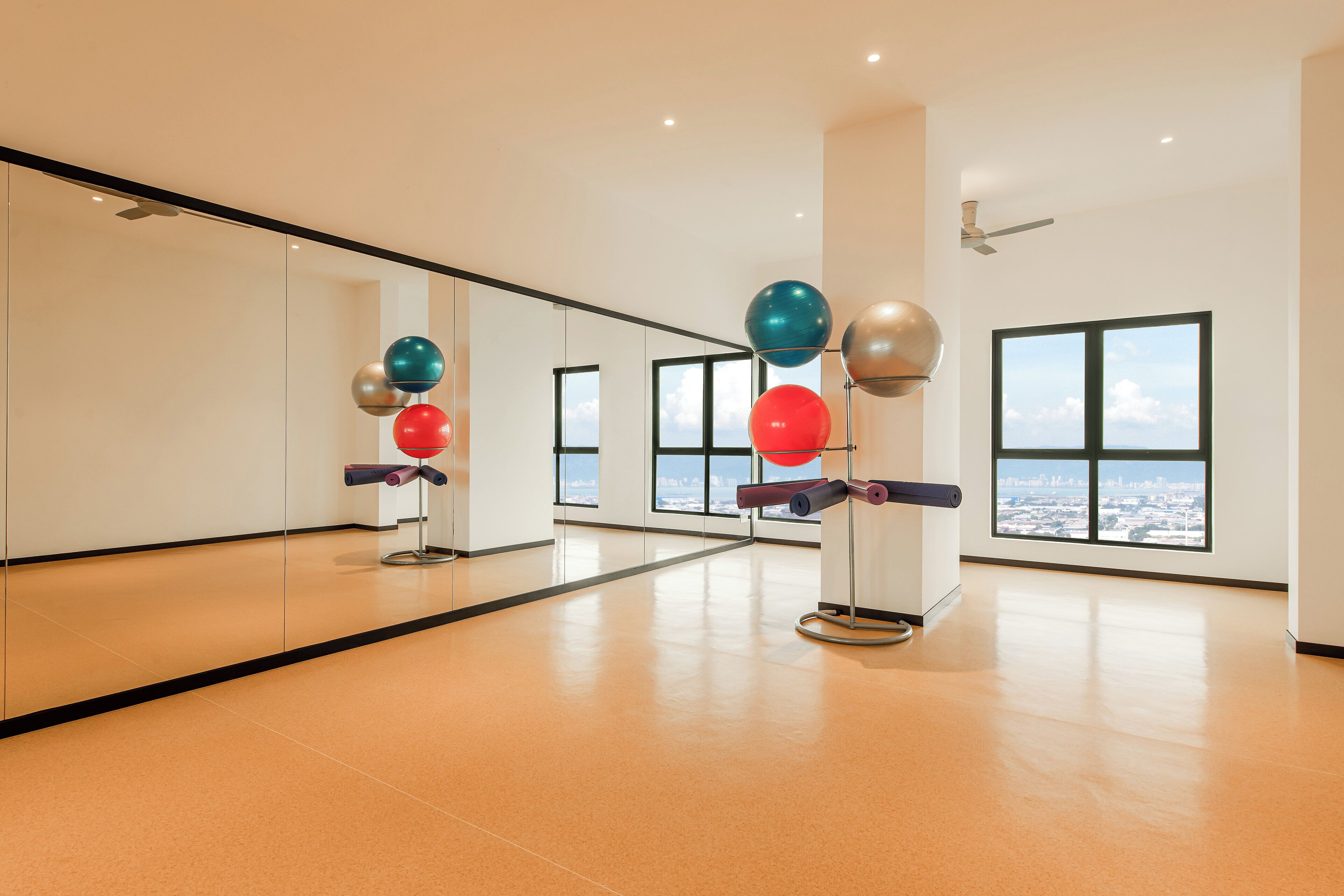 A spacious room with large windows offering a city view, a ceiling fan, and exercise equipment.