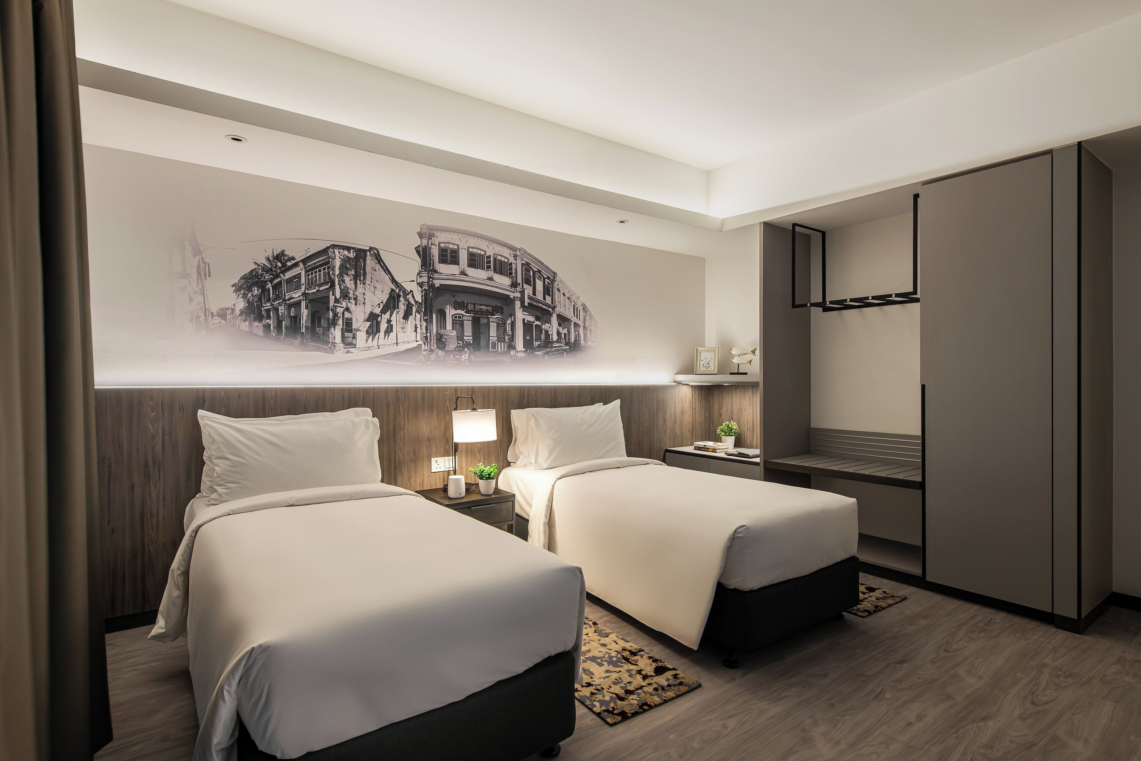 A hotel room with two beds, a wall-mounted TV, a wooden headboard, a nightstand with a lamp, and a large wall mural.