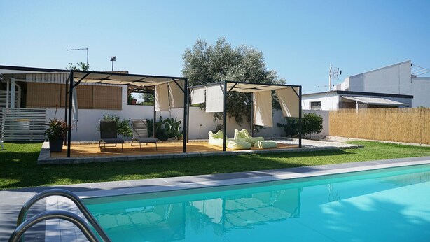 A swimming pool with a covered patio area, outdoor furniture, and a well-maintained lawn. - Dependance in Villa con Piscina by Wonderful Italy (Siracusa)