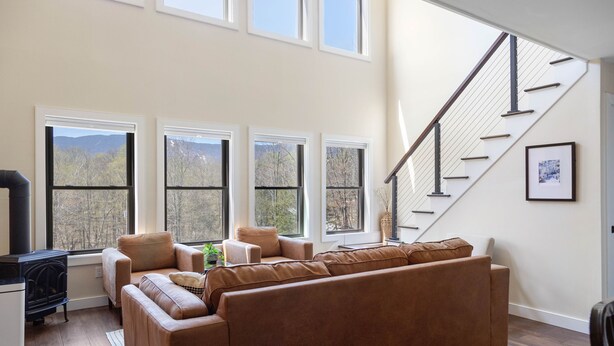 A spacious living room with a large sectional sofa, a fireplace, and a staircase leading to an upper level. - Modern Retreat with Apartment and Mountain Views! (Waitsfield)