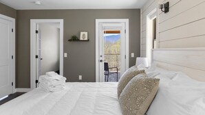 A bedroom with a bed, a stack of towels, a nightstand, and a view of the outdoors through a door. - Modern Retreat with Apartment and Mountain Views! (Waitsfield)
