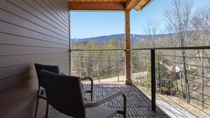 A balcony with a view of mountains and trees, a wicker chair, and a wooden ceiling. - Modern Retreat with Apartment and Mountain Views! (Waitsfield)