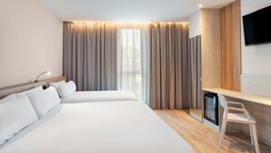 A hotel room with two beds, a desk, a chair, a TV, and a window with curtains. - B&b Hotel Lisboa Montijo (Montijo)