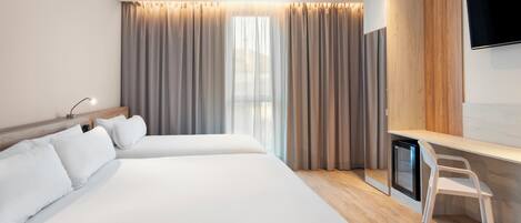 Quarto de hotel com duas camas, uma escrivaninha, uma cadeira, uma televisão e uma janela com cortinas.
