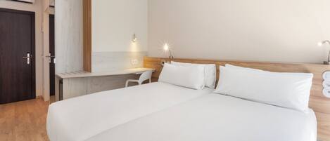 A modern hotel room with a large bed, a desk, and a wardrobe.