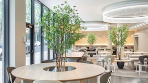 A modern dining area with round tables, chairs, and potted trees.