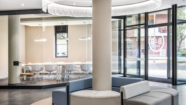 A modern lobby with a curved seating area, a large pillar, and a glass wall with a view of the street.