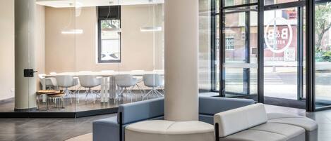 En moderne lobby med et buet siddeområde, en stor søjle og en glasvæg med udsigt til gaden.