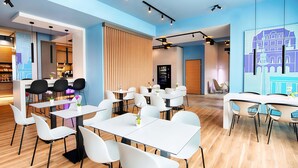 Un restaurante moderno con mesas y sillas blancas, piso de madera y pared azul con un mural de paisaje urbano.