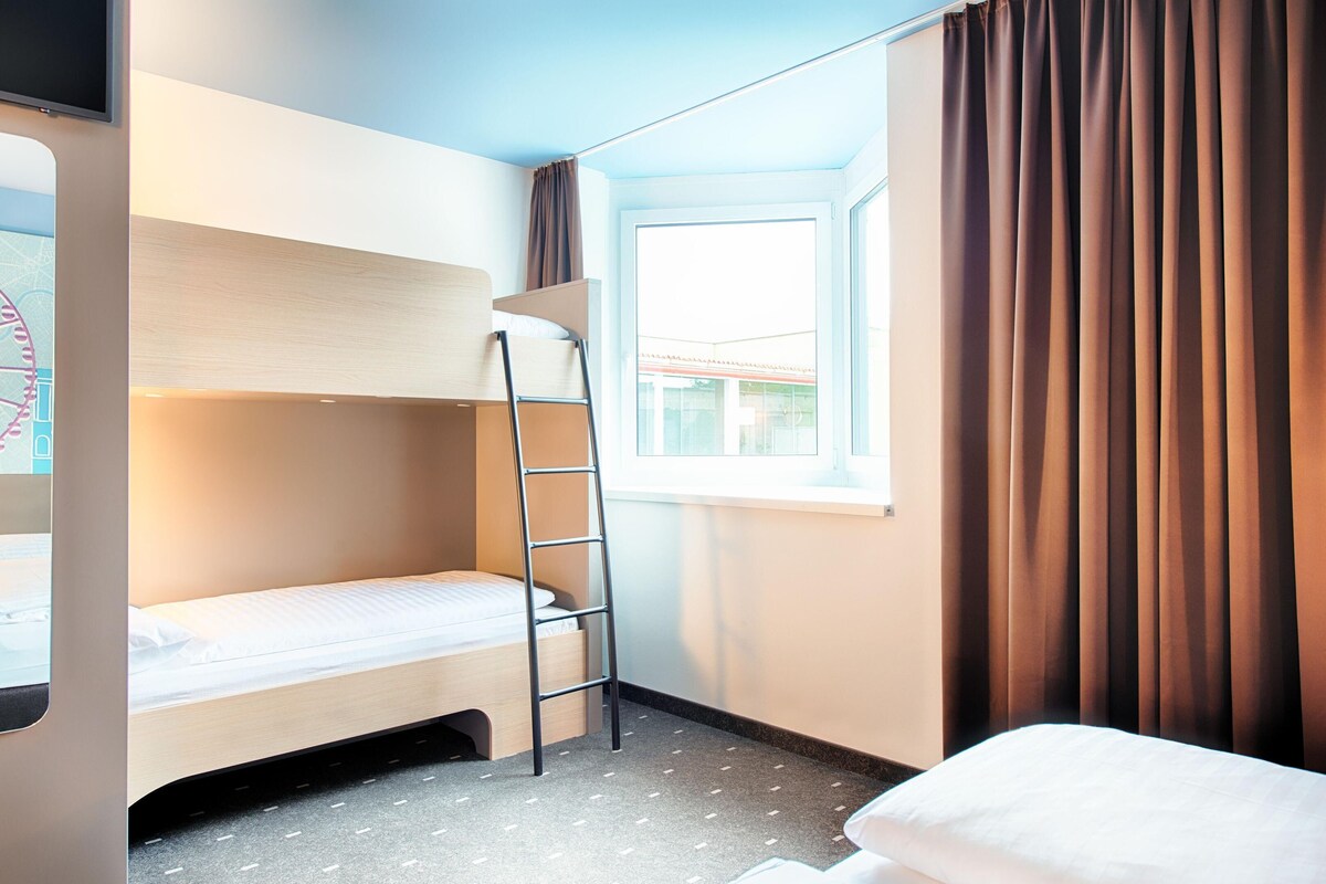 Ein Schlafraum mit Etagenbett, einer Leiter, einem Fenster mit Vorhängen und Blick ins Freie.