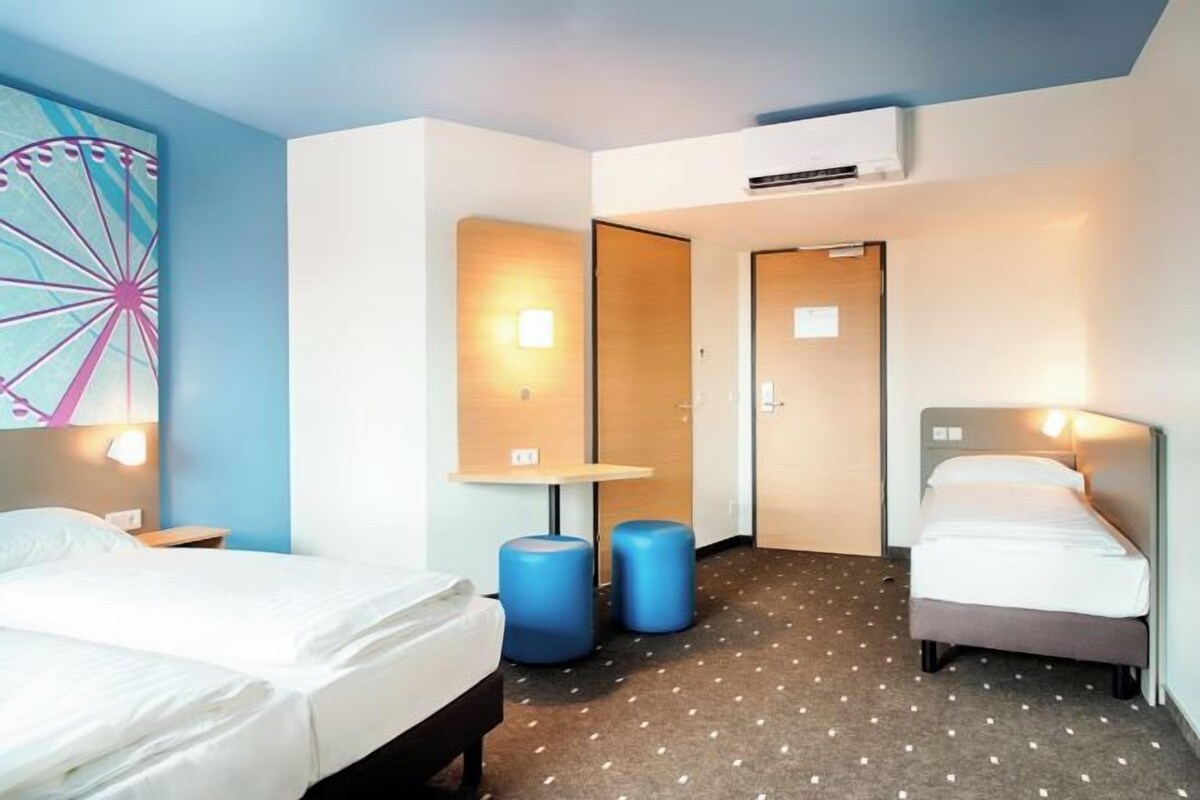 A hotel room with two beds, a large wall clock, and a door leading to another room.