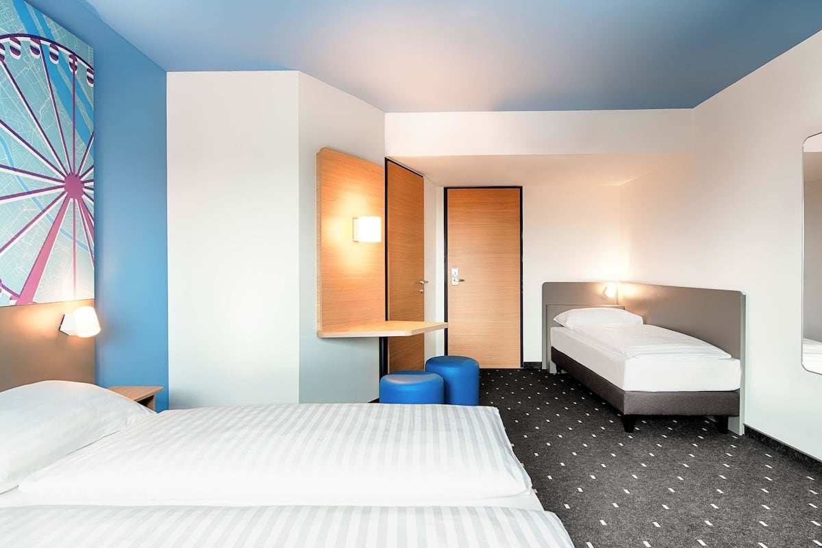 A hotel room with a bed, a desk, a chair, and a wall-mounted lamp.