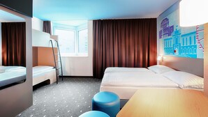Una habitación de hotel con literas, un escritorio, una silla, una ventana y una obra de arte en la pared.