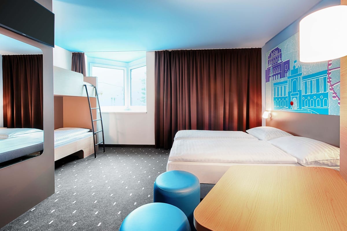 A hotel room with bunk beds, a desk, a chair, a window, and a wall art piece.