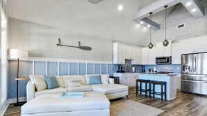 A modern kitchen with white cabinets, a stainless steel refrigerator, and a bar area with stools. - Luxury Beach Front Home!!! (Long Beach)