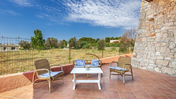 An outdoor patio with wicker furniture, a white table, and a stone wall. - Spacious apartment just minutes from the beaches of the Maldives of Salento (Pescoluse)