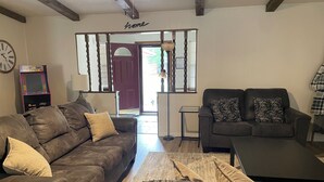 A living room with a brown leather sofa, a black sofa with patterned pillows, a small table, and a clock on the wall.