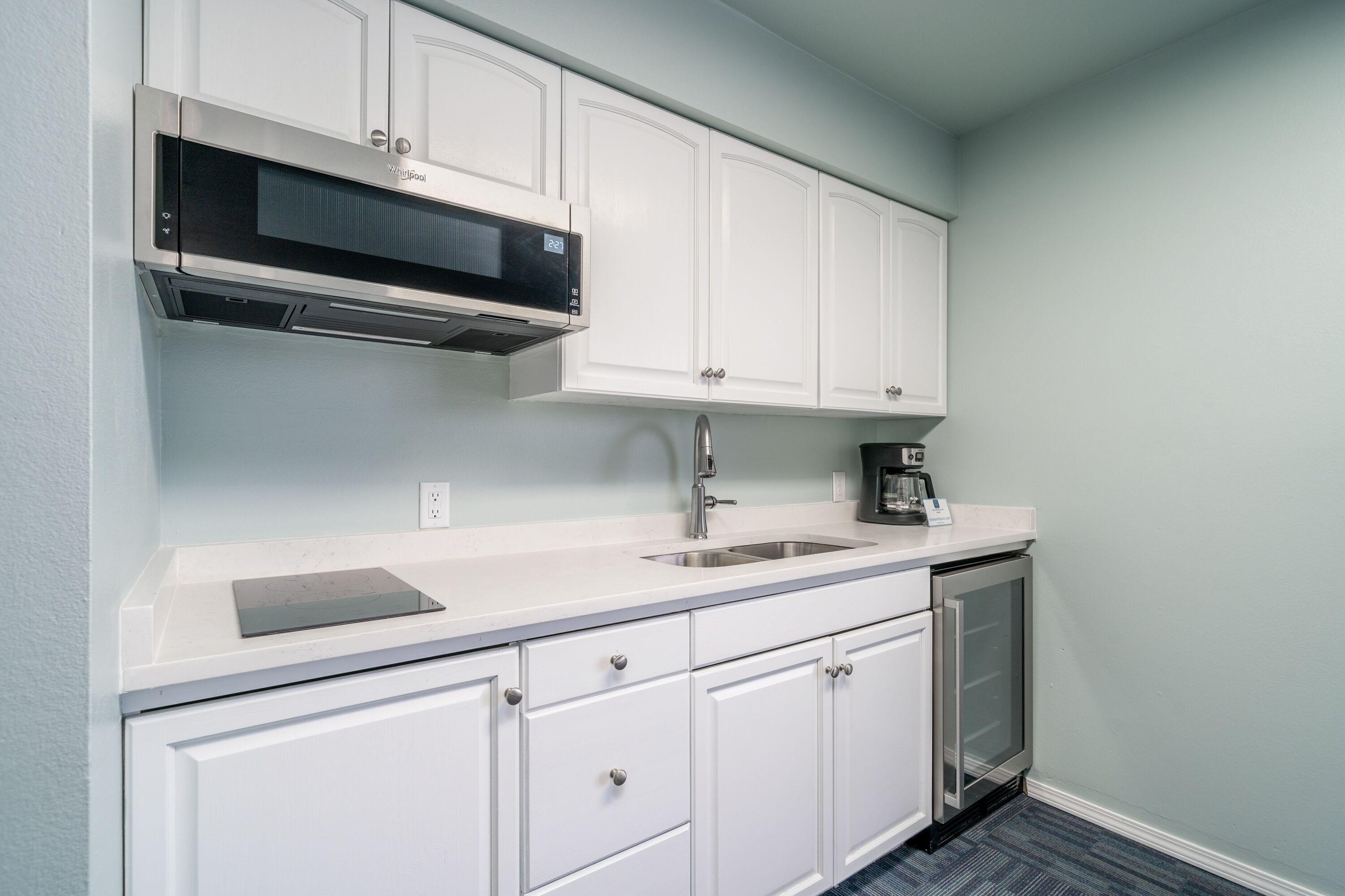 A modern kitchen with white cabinets, a built-in microwave, a sink, and a coffee maker.