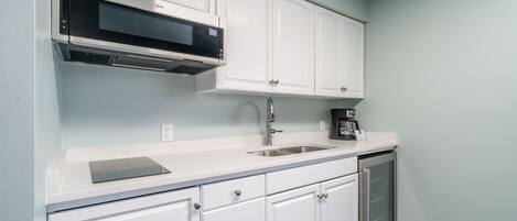 A modern kitchen with white cabinets, a built-in microwave, a sink, and a coffee maker.