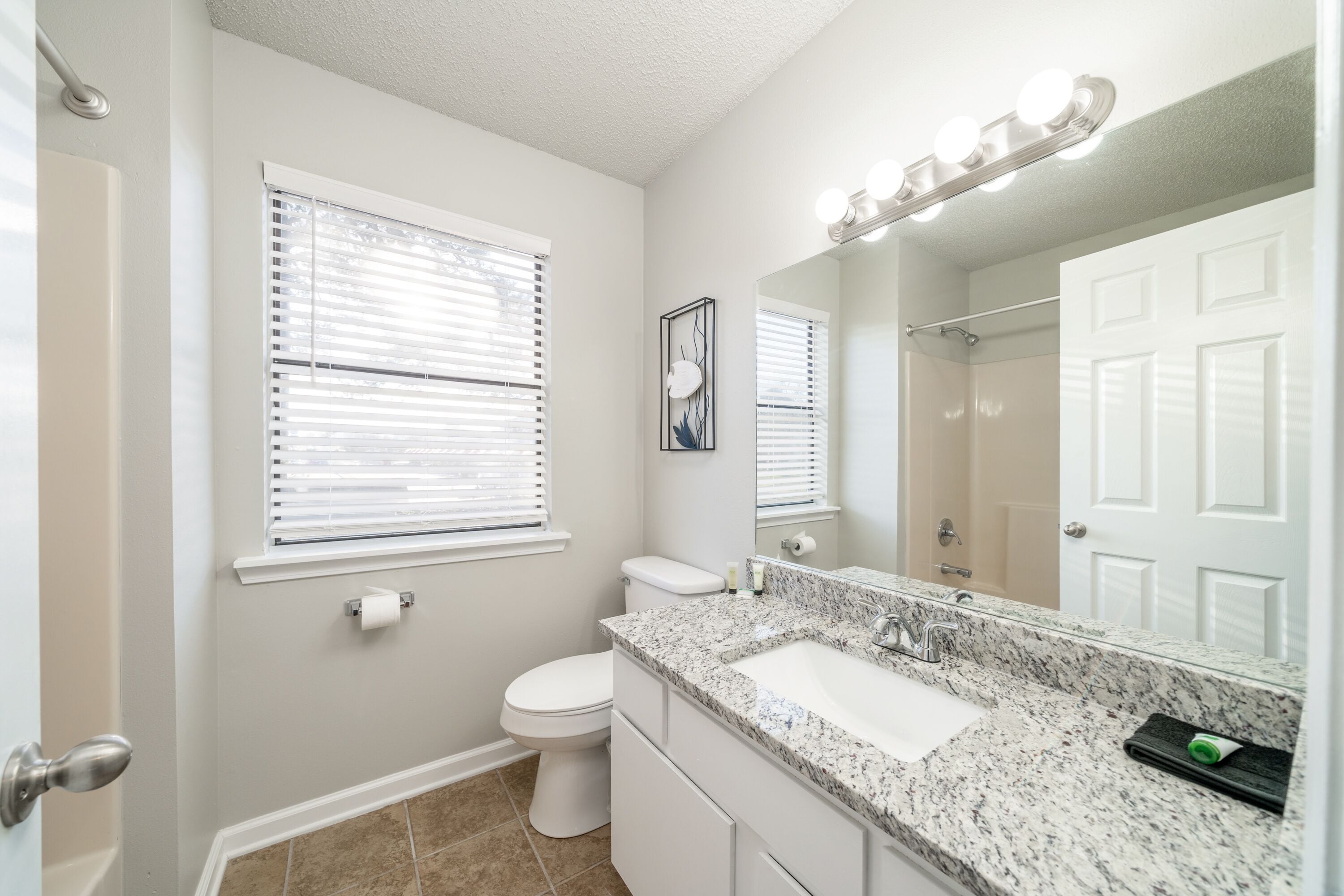 A bathroom with a white toilet, a sink with a marble countertop, and a large mirror with lights above it.